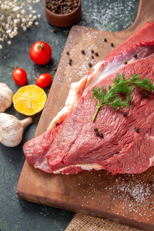 front-close-view-fresh-raw-red-meat-wooden-cutting-board-nude-color-towel-lemon-garlic-mixed-color-background 1-min